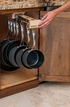 a person is holding pots and pans in a kitchen cabinet that has drawers on both sides