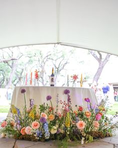 a table with flowers and candles on it under a white tent at an outdoor event