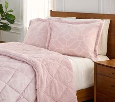 a bed with pink comforter and pillows on it in a room next to a plant