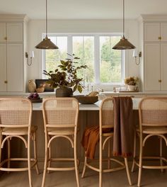 a kitchen with white cabinets and wooden stools next to an island in front of a window