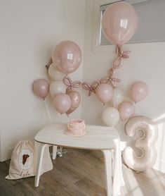 a table topped with pink and white balloons next to a number 3 cake on top of a wooden table