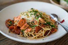 a white plate topped with pasta covered in sauce and meats next to a fork