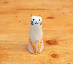 a small white cat figurine sitting on top of a wooden table next to a piece of wood