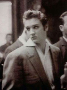 black and white photograph of a man in suit with other men standing around behind him