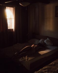 a person laying on top of a bed in a dark room next to a window