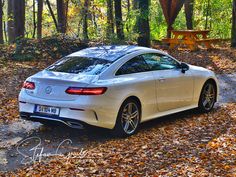 a white sports car parked in the woods near a picnic table with an orange bench