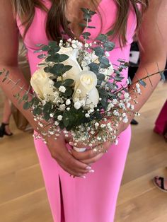 a woman in a pink dress holding a bouquet of white roses and baby's breath