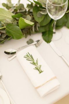 the table is set with silverware, napkins, and greenery on it