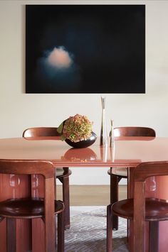 a dining room table with two chairs and a vase on the table in front of it