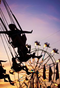 a person on a swing ride in front of a ferris wheel at sunset or dawn