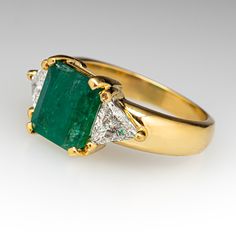 This beautifully designed ring is centered with one (1) emerald cut natural emerald set into a four-prong setting. Each shoulder is accented with one (1) triangular modified brilliant cut diamond set into a three-prong setting. The ring measures 9.9mm at the top, rises 5.8mm above the finger, and tapers to 2.8mm wide by 1.0mm thick at the base of the shank.  It is currently a size 6.5. Luxury Trillion Cut Emerald Ring For Formal Occasions, Luxury Gia Certified Trillion Cut Emerald Ring, Luxury Gia-certified Trillion Cut Emerald Ring, Luxury Trillion-cut Emerald Ring, Luxury Trillion Cut Diamond Emerald Ring, Luxury Trillion Cut Emerald Diamond Ring, Luxury Trillion Cut Emerald Jewelry, Formal Trillion-cut Emerald Jewelry, Trillion Cut Green Diamond Ring