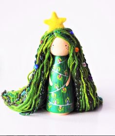 a wooden doll with green dreadlocks and a yellow star on her head, sitting in front of a white background