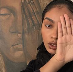 a woman holding her hand to her face in front of a wall with a painting on it