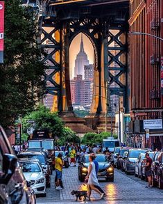 people are walking down the street in front of cars and a bridge that is lit up