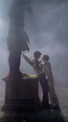 two people standing in front of a statue that looks like a giant creature with wings