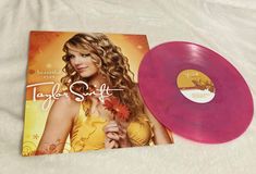 a pink vinyl record sitting on top of a white bed next to an album cover