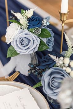 blue and white flowers are sitting on a table with gold candlesticks in the background