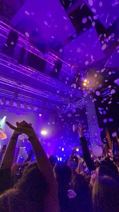 people are throwing confetti in the air at a party with purple lights and blue lighting