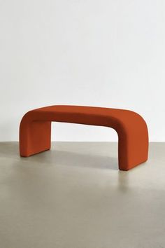 an orange curved bench sitting on top of a cement floor next to a white wall