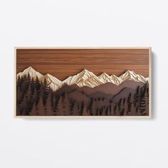 a wooden wall hanging with mountains and trees on it