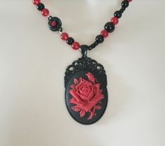 "Red Rose Necklace This beautiful necklace has red glass beads, black glass beads, seed beads, black metal connectors with rhinestones, black metal chain and a black metal pendant with resin rose. 20\" long. Lobster clasp." Gothic Black Beads Necklace For Gift, Adjustable Gothic Beaded Necklace As Gift, Gothic Black Bead Necklace For Gift, Black Necklace With Rose Design For Gift, Adjustable Gothic Beaded Necklace For Gift, Gothic Beaded Necklace For Gift, Black Necklace With Rose Design As Gift, Vintage Black Necklace For Valentine's Day, Gothic Rose Colored Jewelry For Gift