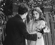 a man and woman standing next to each other in front of a fence with flowers