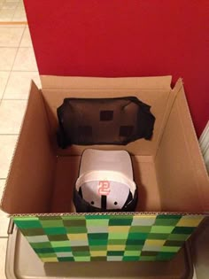 an open cardboard box with a white and black object in it sitting on the floor next to a red wall