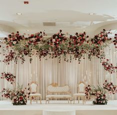 an elegant wedding setup with red flowers and greenery on the wall, along with white chairs