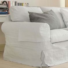 a white couch with pillows on it in front of a bookshelf and window