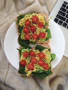 two pieces of bread with tomatoes and avocado on them next to a laptop