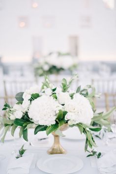 white flowers are in a gold vase on a table set for an elegant wedding reception