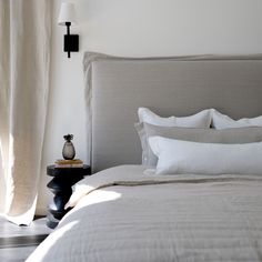 a bed with white sheets and pillows next to a wall mounted light on the side