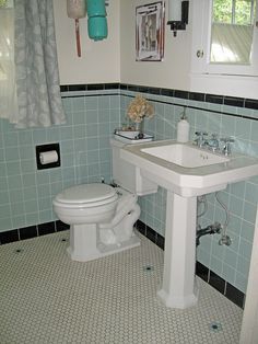 a white toilet sitting next to a sink in a bathroom under a window with blue tiles on the walls