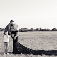 a black and white photo of a pregnant woman with her husband standing in a field