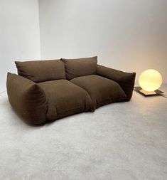 a brown couch sitting on top of a white floor next to a light that is turned on