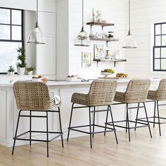 three wicker bar stools in front of an island with shelves on the wall