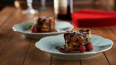 two plates with desserts on them sitting on a wooden table next to wine glasses