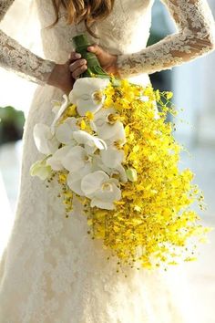 a bride holding a bouquet of yellow and white flowers on her wedding day with lace sleeves