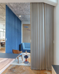 an open room with blue curtains and chairs in it, next to a wooden table