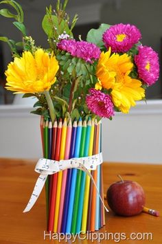 a vase filled with colorful flowers next to an apple and pencils on a table