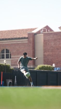 a young man kicking a soccer ball on top of a field in front of a building