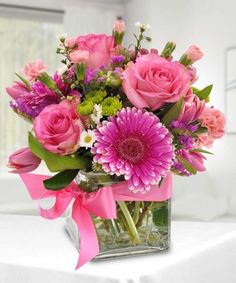 a vase filled with pink and purple flowers on top of a white table next to a window