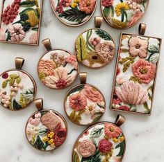 nine embroidered pendants with flowers on them sitting on a marble counter top, all in different colors