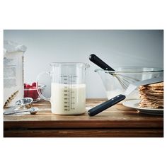 a wooden table topped with measuring cups filled with milk and other items next to each other