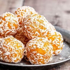 a plate filled with orange coconut balls on top of a wooden table