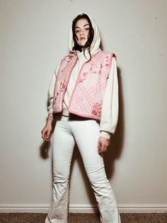 a woman standing in front of a wall wearing white pants and a pink jacket