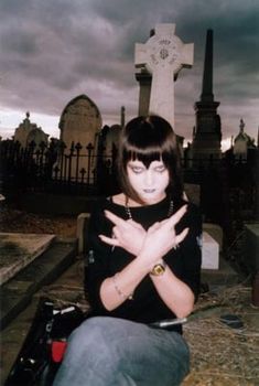 a woman sitting in front of a grave with her hands clasped up to her chest