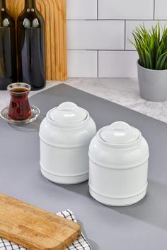 two white canisters sitting on top of a counter next to a cutting board