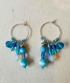 These whimsical, hand crafted, one of a kind earrings are made with silver plated copper wire hoops with aqua blue glass beads and mother of pearl beads.  Assorted beads dangle from the beaded hoops, adding shimmer to the unique earrings.  They sparkle in the sun adding a touch of fun to your look!  All earring hooks are made of high quality material, nickel-free, Hypo-allergenic, safe and durable.  Earrings are approximately 2" long. The beautiful bohemian/hippie style multi-toned earrings woul Bohemian Hippie Style, Gifts Under 25, Boho Hoop Earrings, Beachy Boho, Bohemian Hippie, Beaded Hoops, Earring Hooks, Beaded Dangles, Beach Jewelry