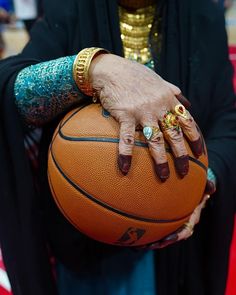 an old woman holding a basketball in her hand with gold rings on it's fingers